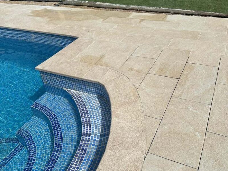 Escalera curva de piscina revestida en gresite azul con coronación de piedra
