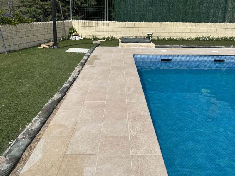 Piscina terminada con solado perimetral de porcelánico y césped en chalet de Madrid